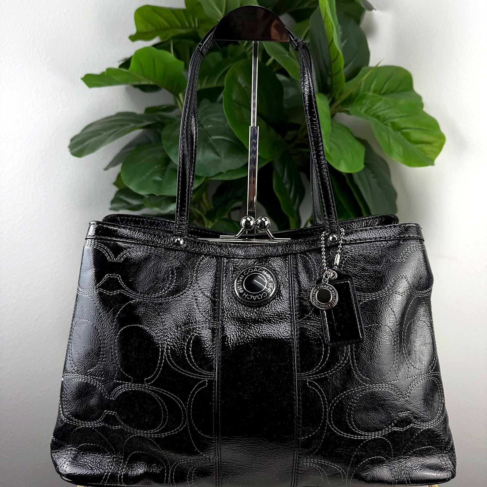 Coach black patent leather tote, angled view showing fob tag and kiss-lock hardware