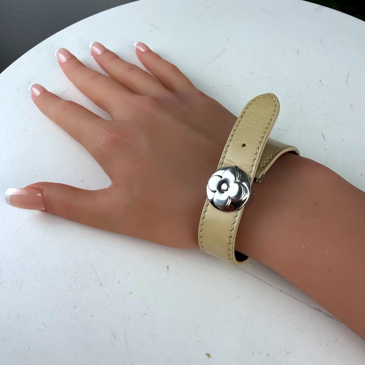 Authentic Louis Vuitton cream Monogram leather bracelet with silver flower snap closure, worn on wrist
