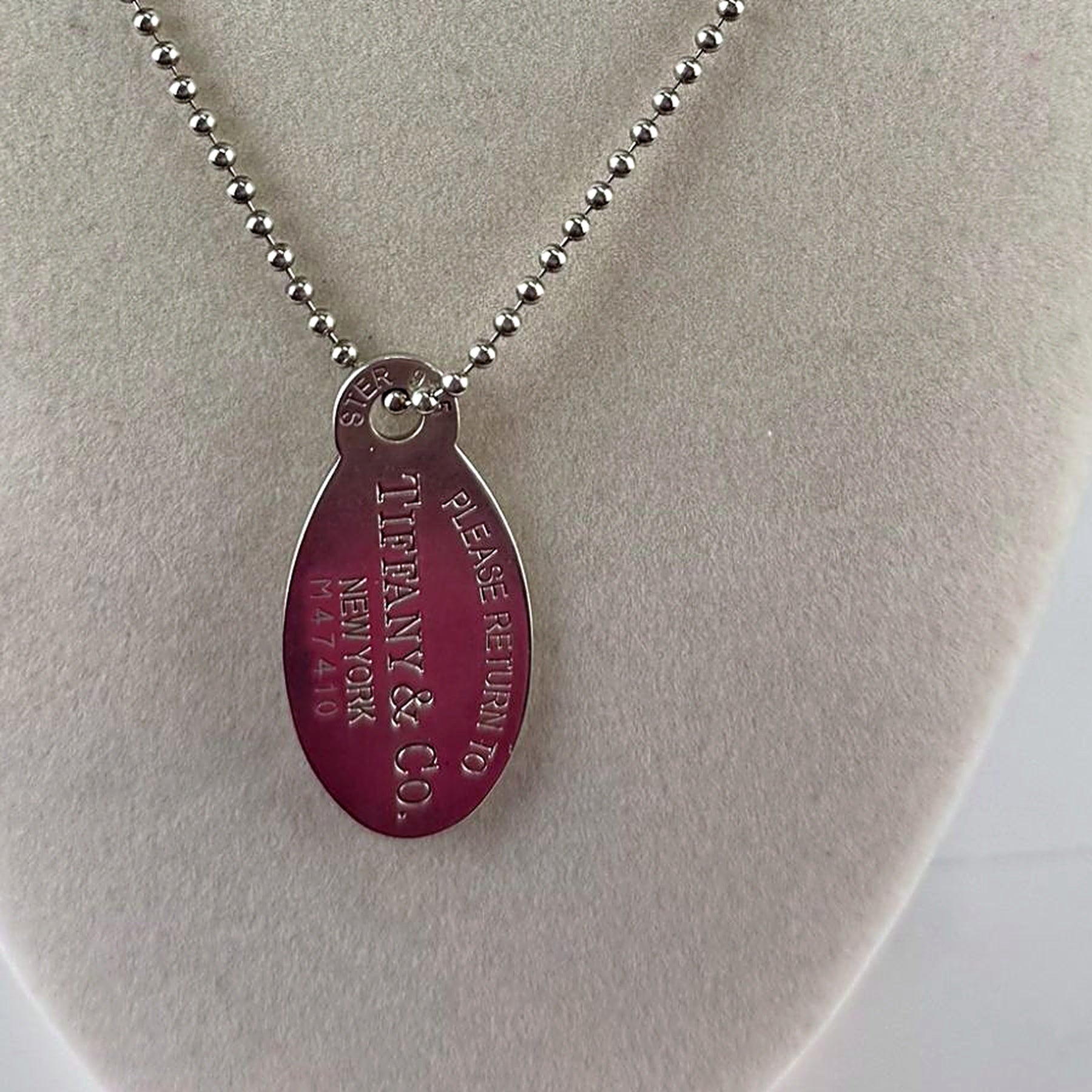 Close-up of Tiffany & Co. Return to Tiffany oval tag engraving reading PLEASE RETURN TO TIFFANY & CO. NEW YORK M47410